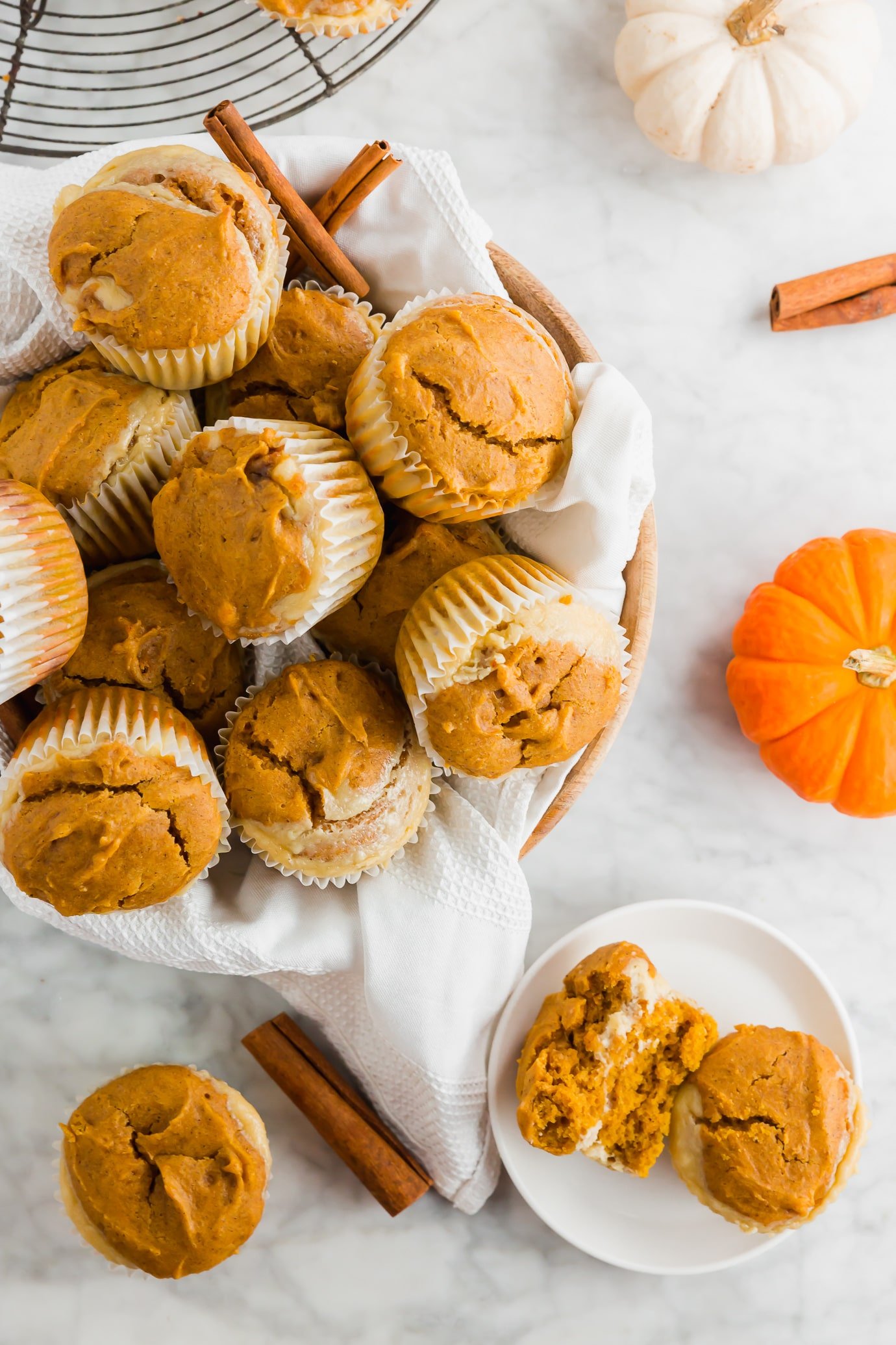 A basket of gluten-free pumpkin cream cheese muffins with fresh pumpkins and cinnamon sticks.