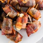 A photo of 3-ingredient bacon wrapped dates with goat cheese with toothpicks inserted in the center on a platter.