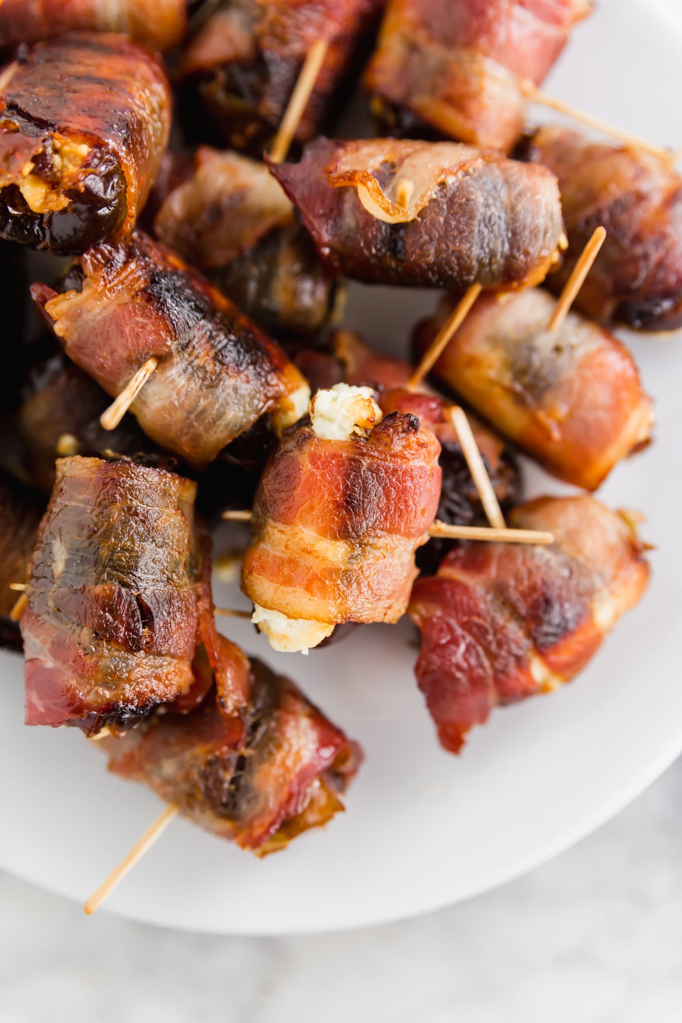 A photo of 3-ingredient bacon wrapped dates with goat cheese with toothpicks inserted in the center on a platter. 