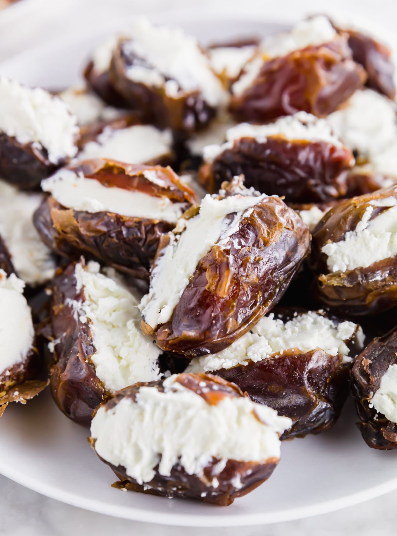 A photo of medjool dates stuffed with goat cheese on a white plate.