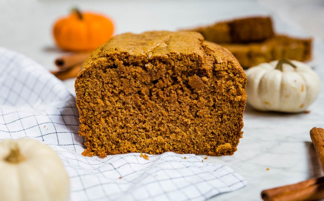 A loaf of gluten-free pumpkin bread with fresh pumpkin and cinnamon sticks. 
