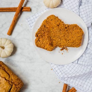Two slices of one-bowl pumpkin bread on a plate with a loaf of gluten-free pumpkin bread, cinnamon sticks and pure pumpkin.