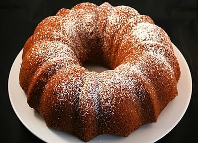 A pear bundt cake dusted with powdered sugar on a white plate.