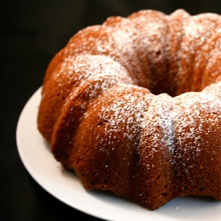 A pear bundt cake sprinkled with powdered sugar on a white plate.