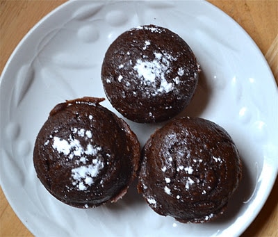 Three peanut butter chocolate muffins sprinkled with powdered sugar on a white plate. 