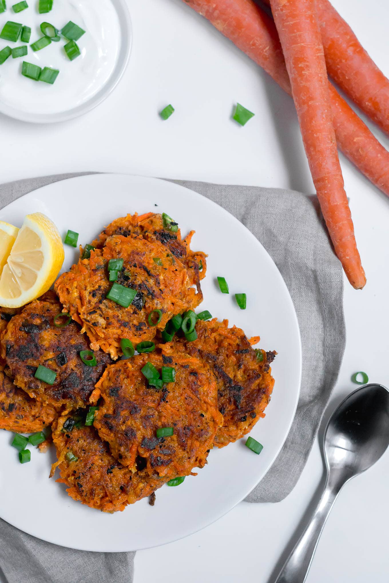 An aerial view of a plate of carrot fritters that are gluten-free with a lemon wedge on a white table. 