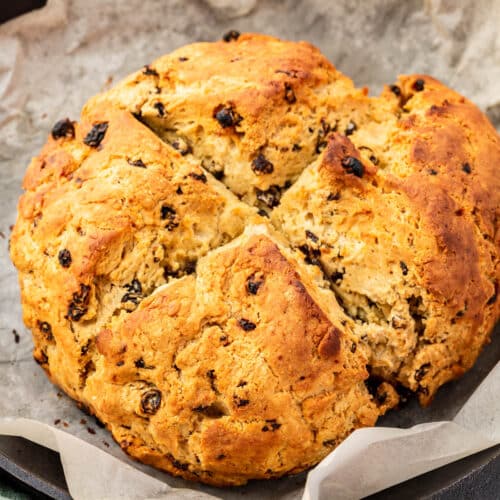 A loaf of gluten-free Irish soda bread in a cast iron skillet lined with parchment paper.