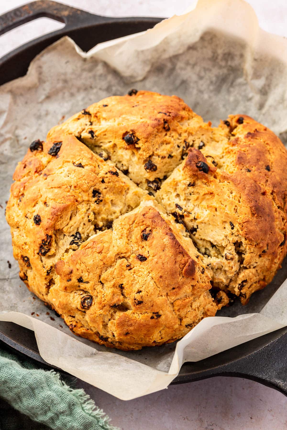 A loaf of gluten-free Irish soda bread in a cast iron skillet lined with parchment paper. 