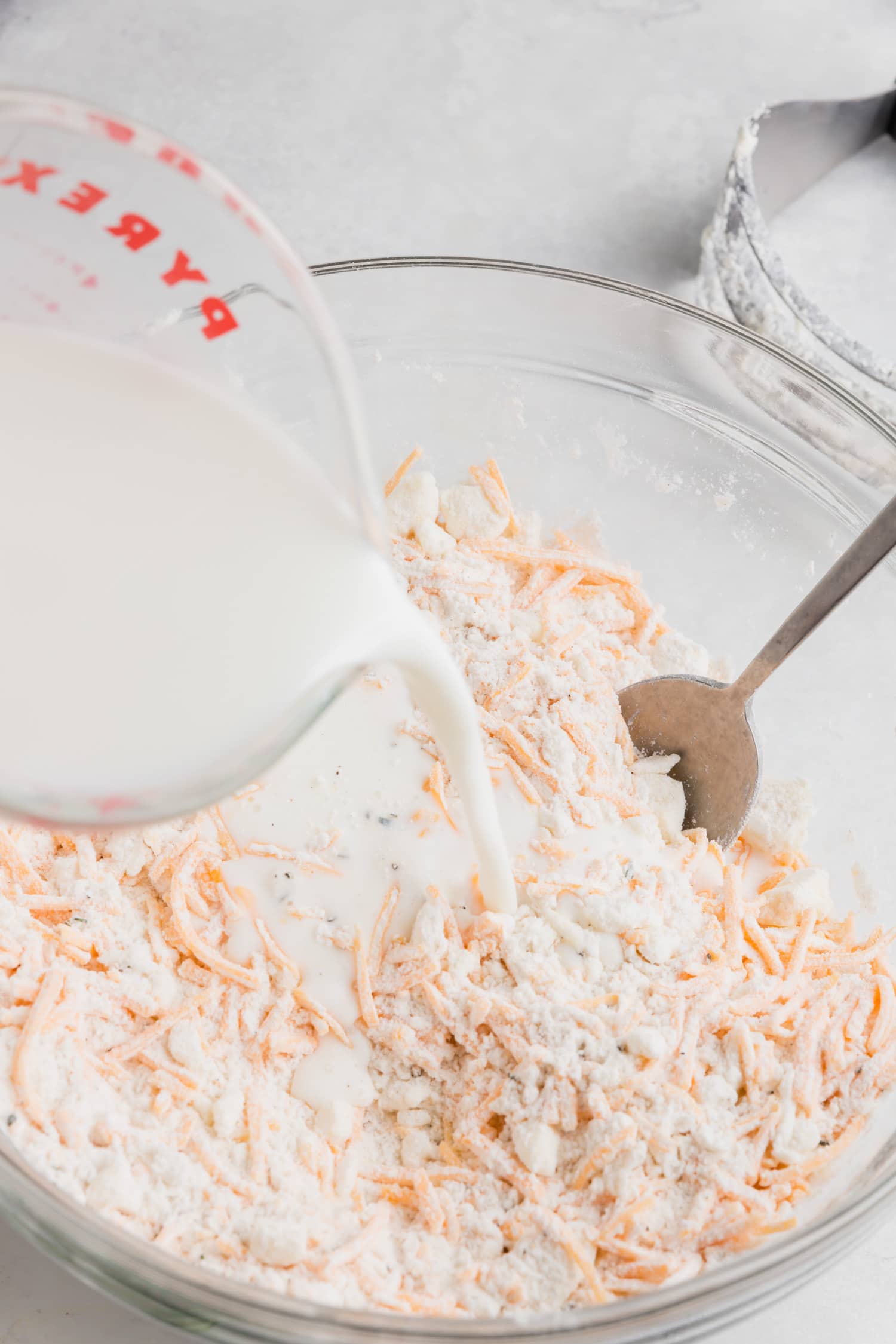 A measuring cup of milk being poured into gluten-free biscuit batter.