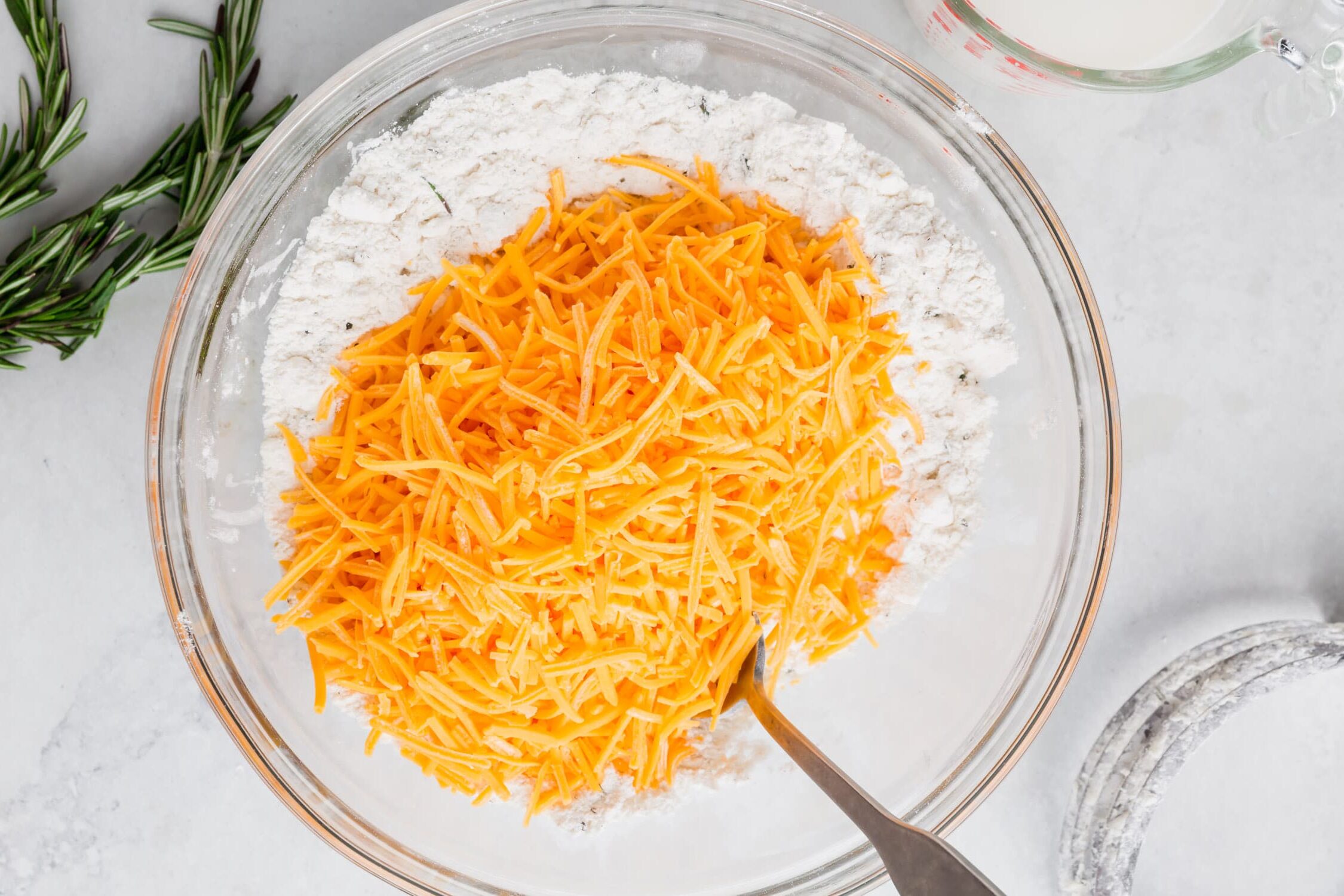 An overhead photo of a bowl of gluten-free flour with shredded cheddar cheese to make cheddar biscuits.