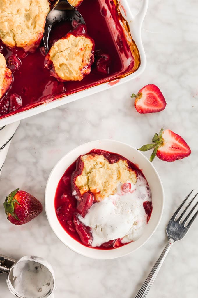 A photo of a bowl of strawberry cobbler with a scoop of melting vanilla ice cream. 