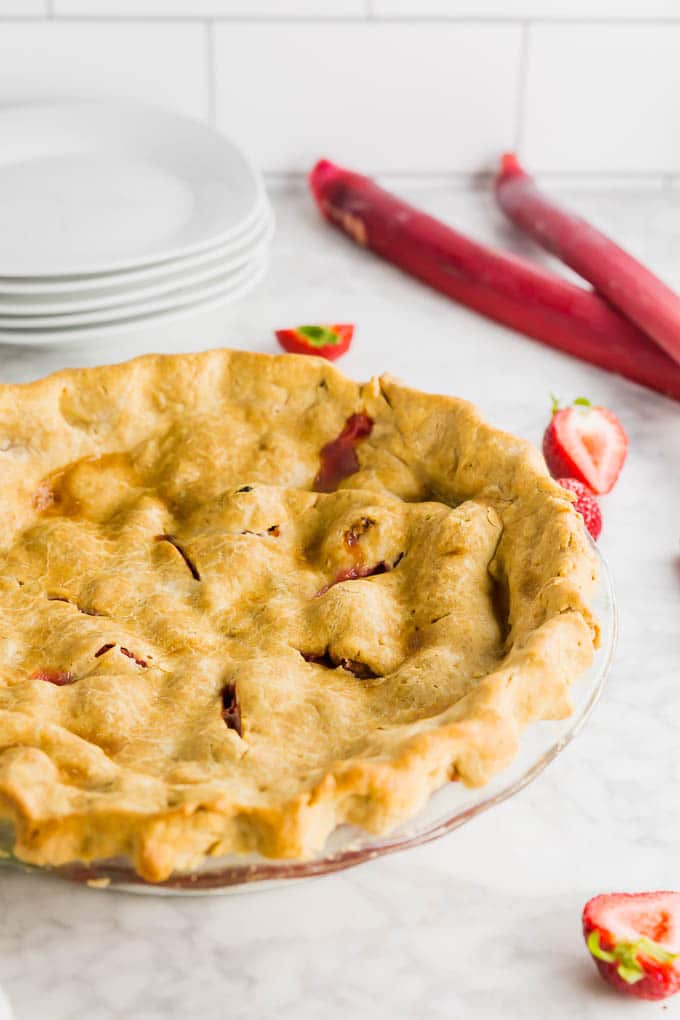 A gluten free rhubarb strawberry pie with a golden brown crust straight from the oven with a stack of plates.