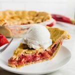 A piece of strawberry rhubarb pie on a plate topped with a scoop of vanilla ice cream.