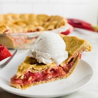 A piece of strawberry rhubarb pie on a plate topped with a scoop of vanilla ice cream.