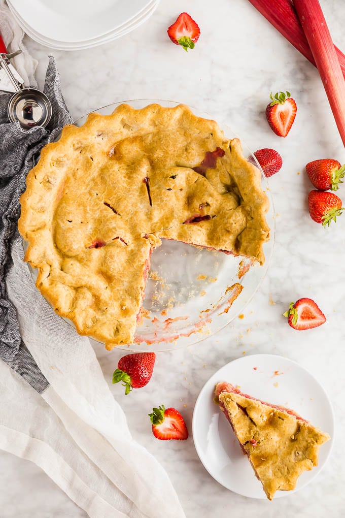 A photo of a gluten free strawberry rhubarb pie with a slice cut out of the whole pie and placed on a plate with a fork.