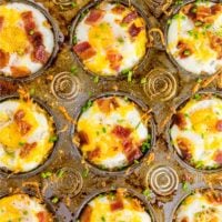 A photo of a muffin tin filled with gluten free hash brown breakfast egg cups topped with bacon, chives and cheddar cheese.