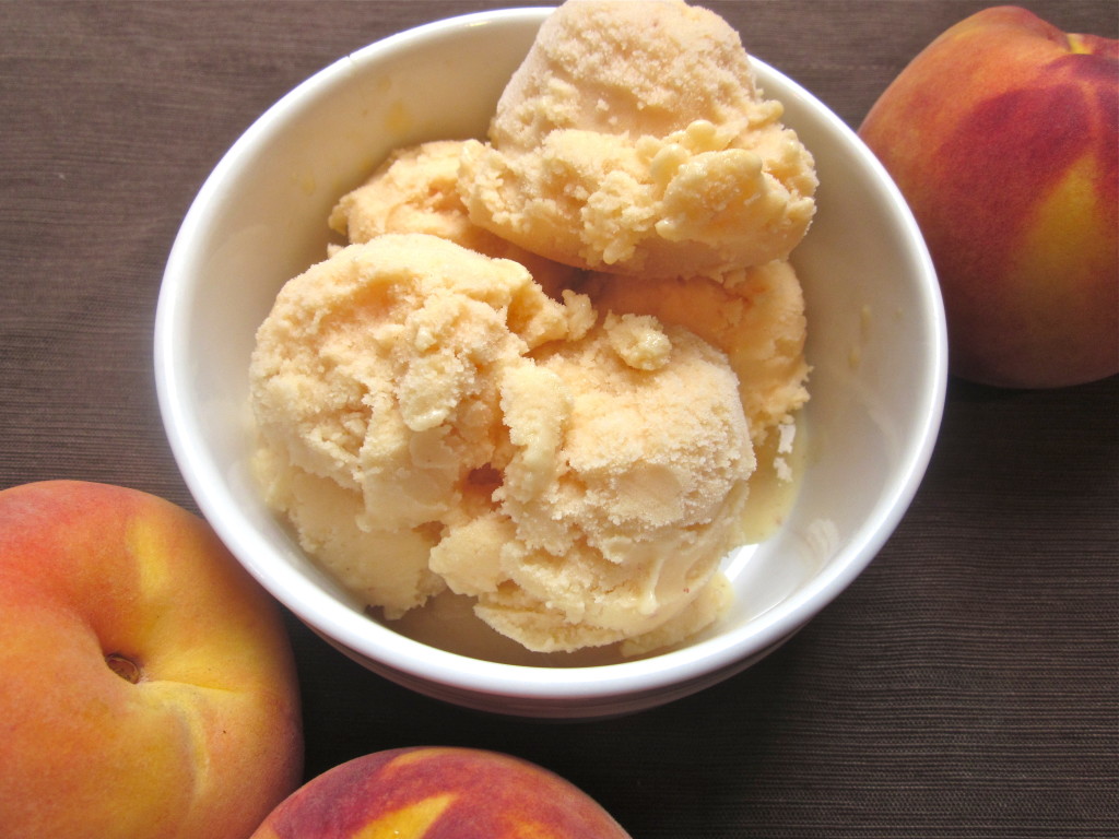 A bowl of peach frozen yogurt with fresh peaches on the side.