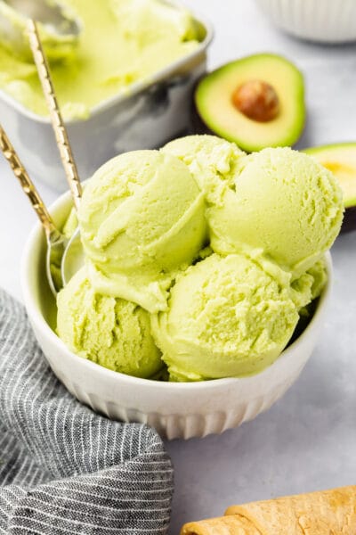 A bowl of avocado ice cream with avocados in the background.