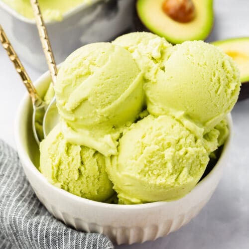 A bowl of avocado ice cream with avocados in the background.