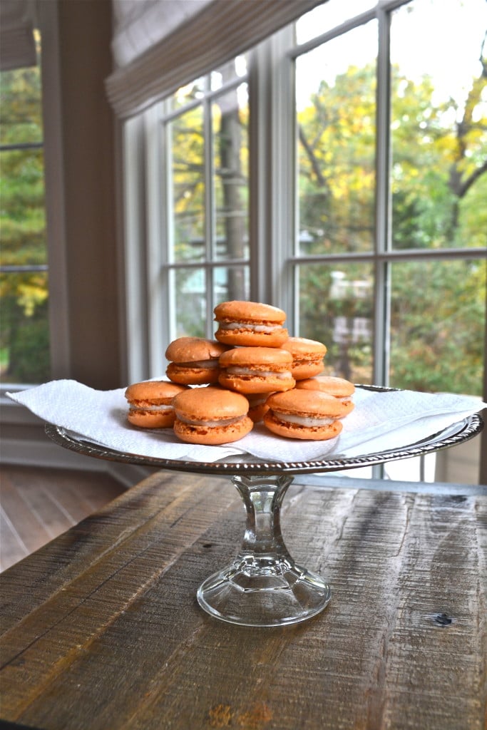 A stack of pumpkin pie macarons with cream cheese filling on a cake stand.