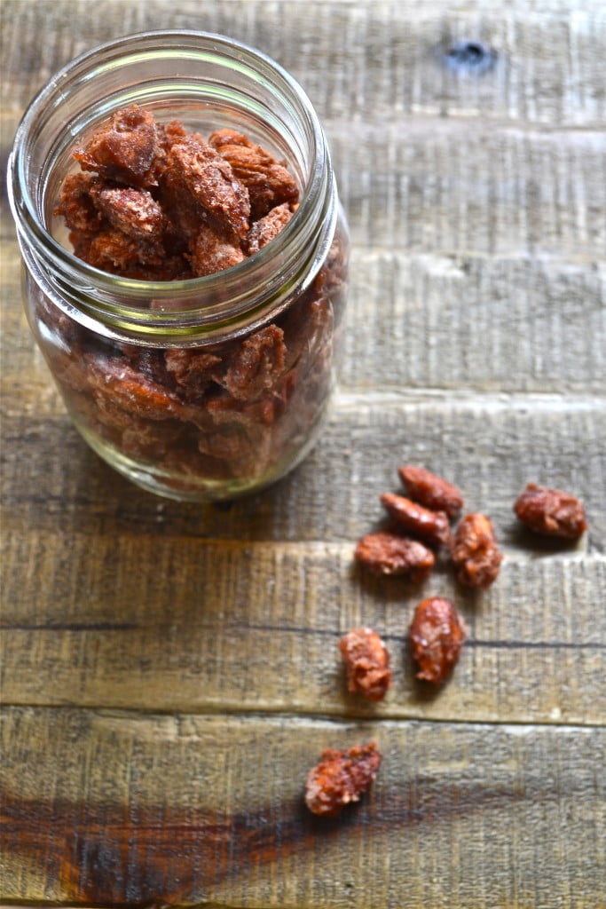 A mason jar of candied almonds with a few almonds on the surface.