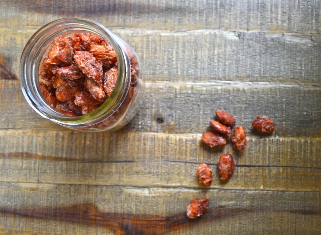 A glass jar of candied almonds with a few almonds on the surface.