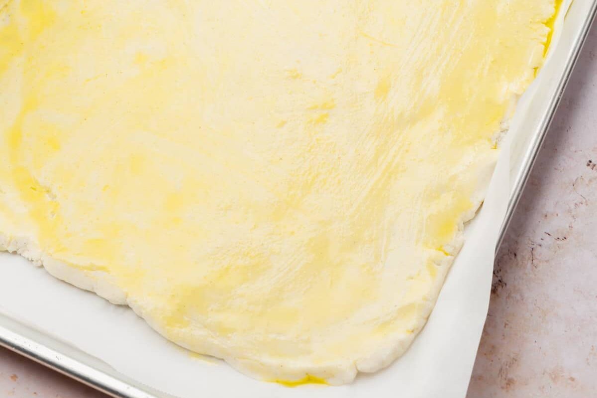 Olive oil brushed on top of gluten-free dough on a baking sheet.