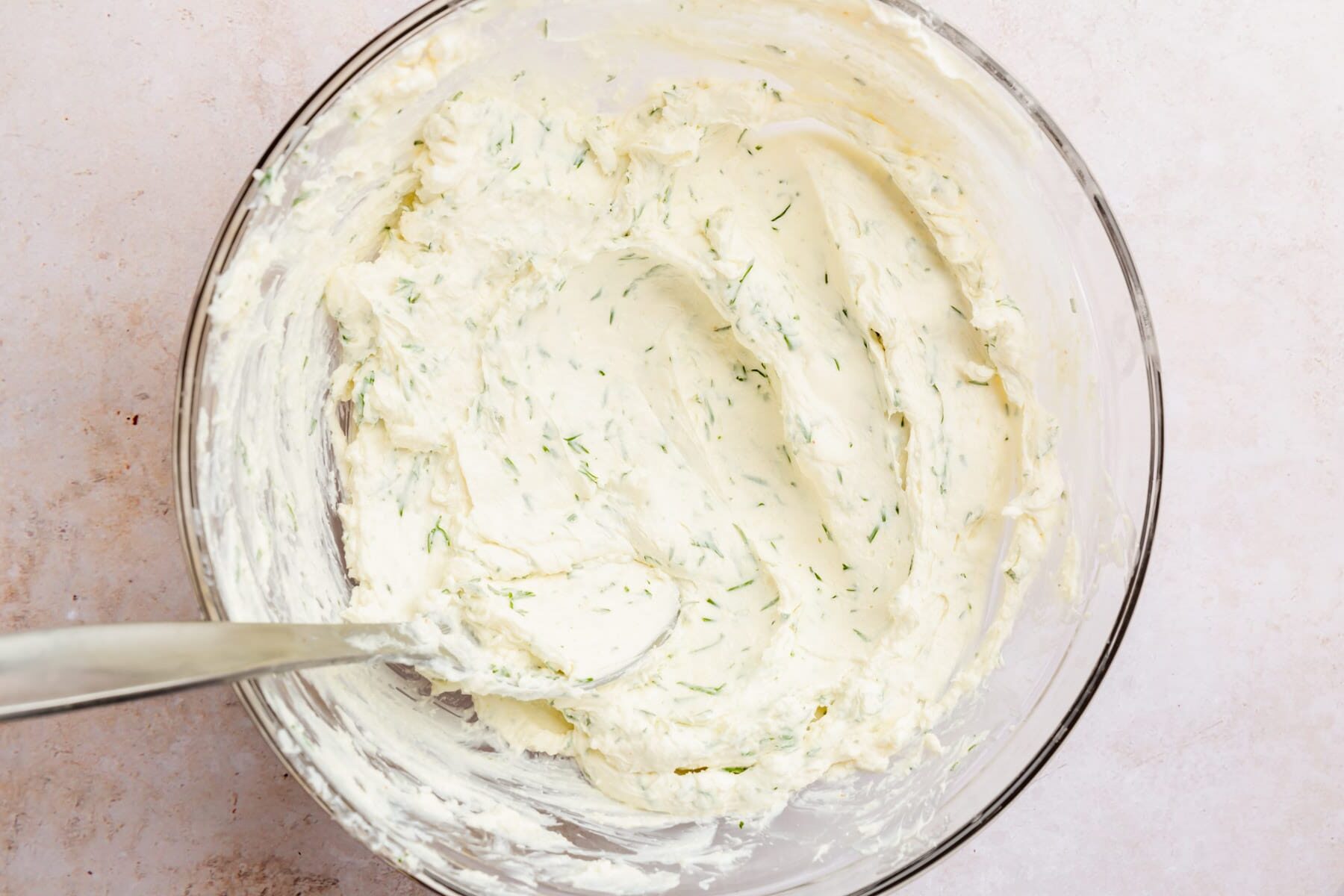 A bowl of softened dill cream cheese with a spoon.