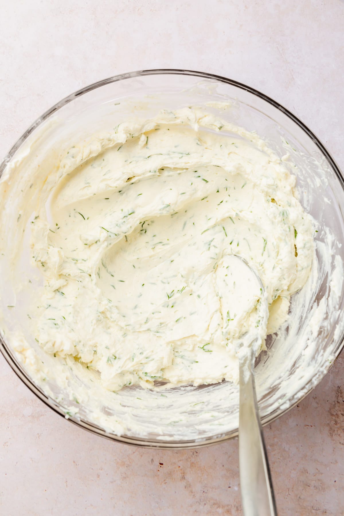 A bowl of softened dill cream cheese with a spoon.