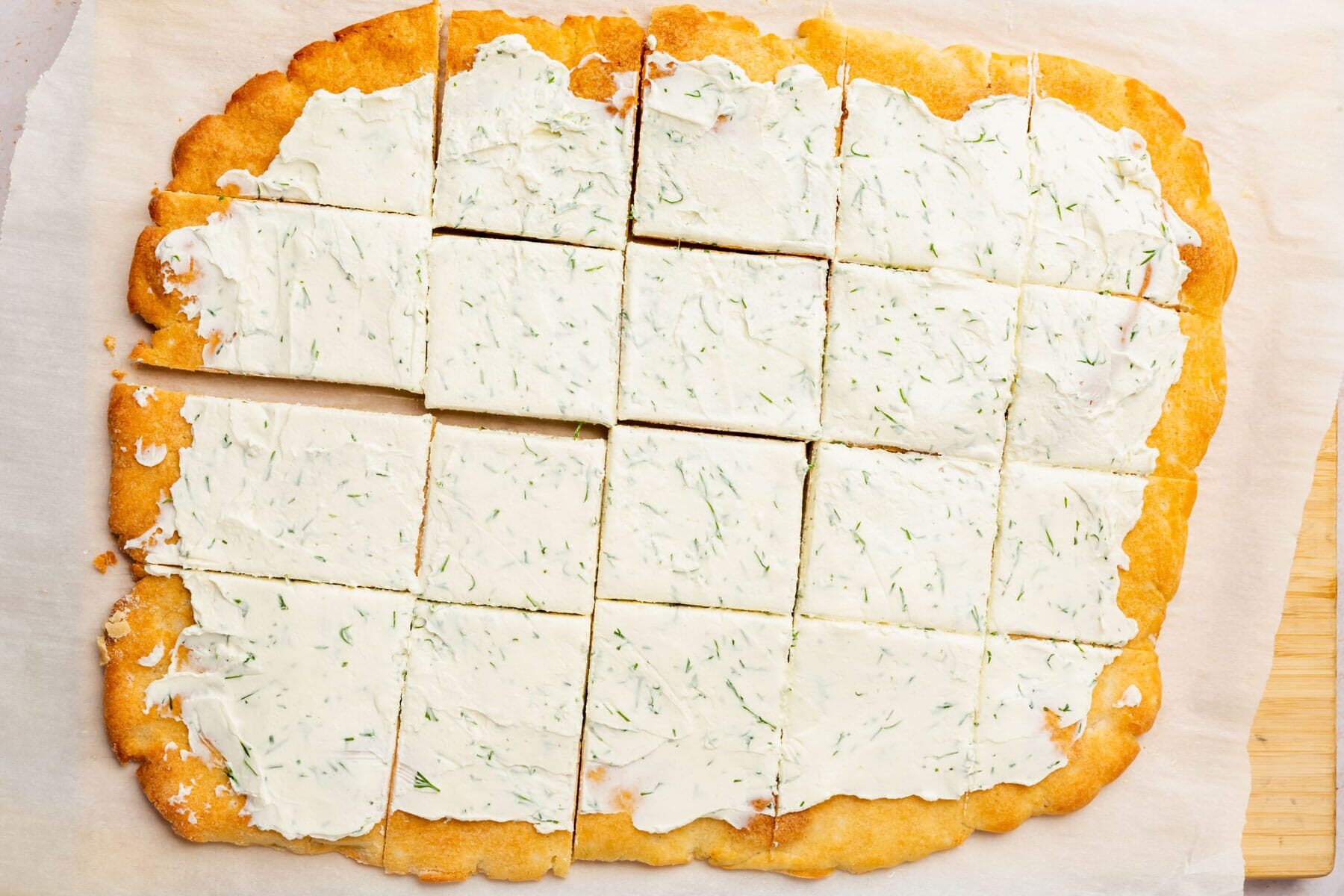 Rectangular gluten-free pizza dough topped with dill cream cheese and cut into 20 squares.