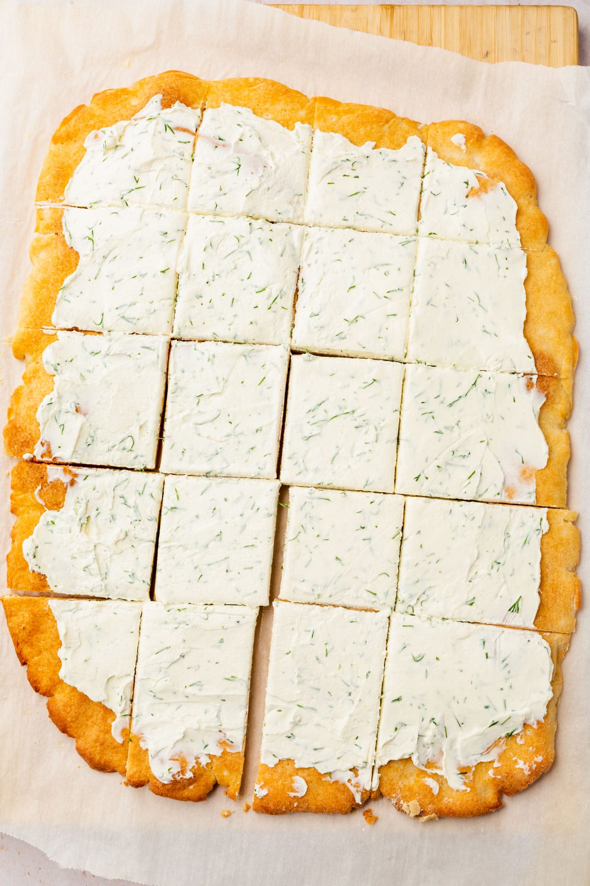 Rectangular gluten-free pizza dough topped with dill cream cheese and cut into 20 squares.
