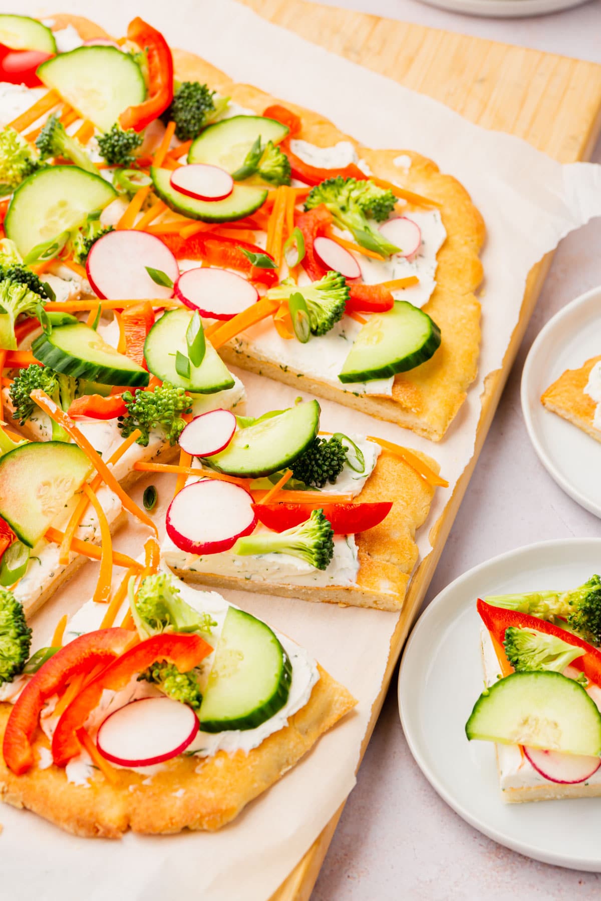 Gluten-free cold veggie pizza on a cutting board with some single servings on plates to the side.