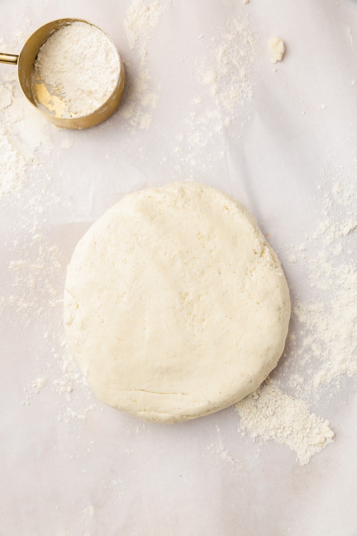 A disk of gluten-free dough on a piece of parchment paper dusted with gluten-free flour.