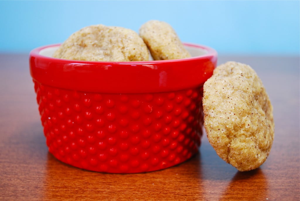 A pile of pumpkin snickerdoodle cookies in a red bowl with one cookie leaning against the bowl. 