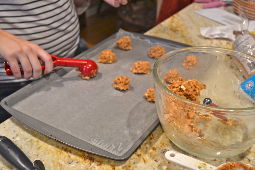 A cookie scoop portioning out peanut butter pretzel filling onto a baking sheet.