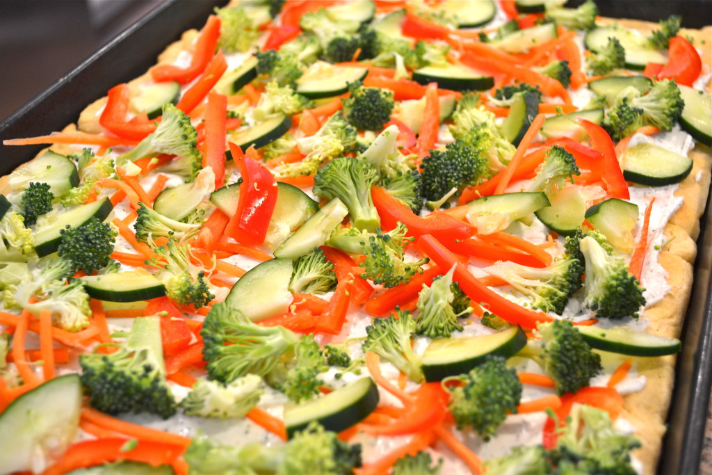 A closeup of cold pizza topped with cucumber, broccoli, pepper and carrots.