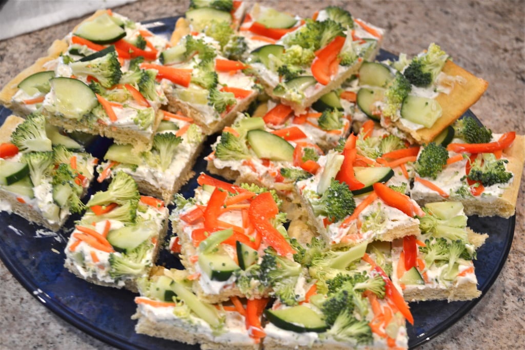 Slices of cold veggie pizza topped with cucumber, peppers, broccoli and carrots on a blue platter.