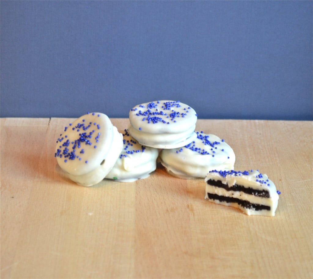 White chocolate covered oreos with blue sprinkles on a wood table.