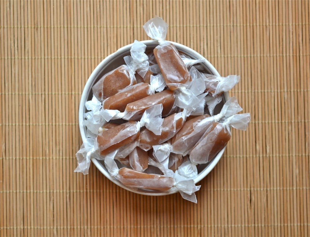 A bowl of apple cider caramels wrapped in wax paper in a bowl.