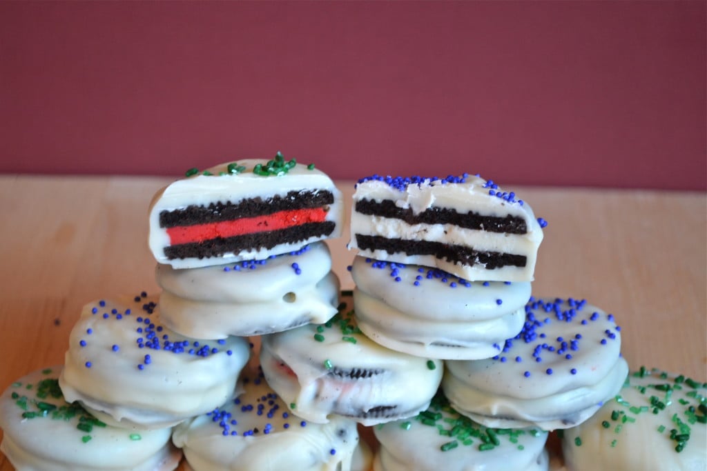 A stack of gluten-free oreos that are covered in white chocolate and green and blue sprinkles.