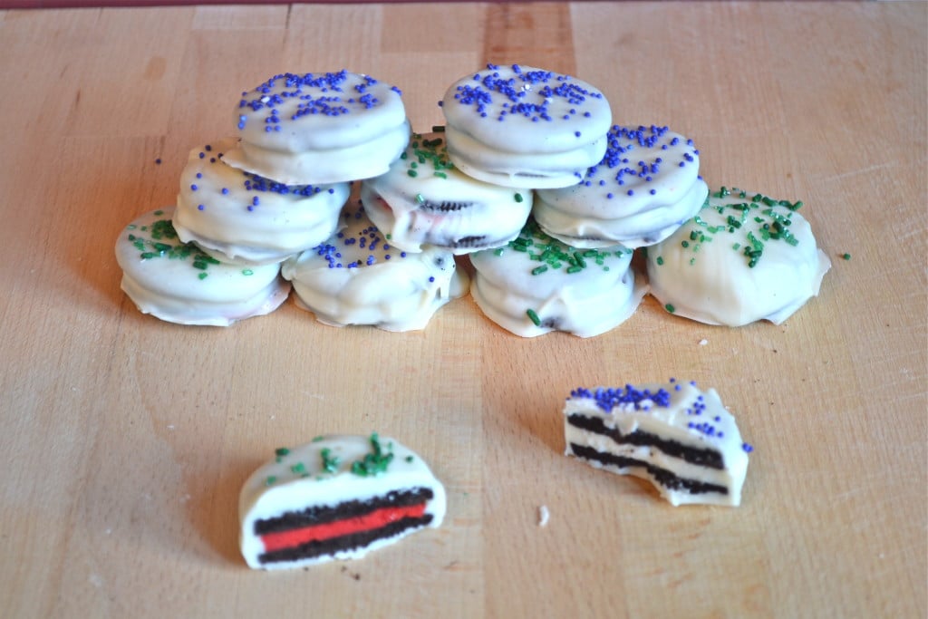 A stack of white chocolate covered oreos with blue and green sprinkles.