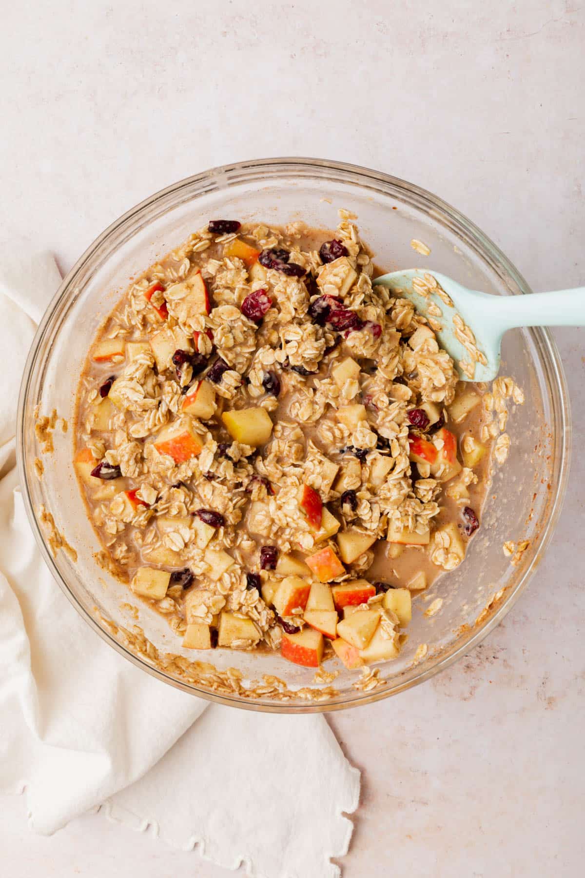 A glass mixing bowl with an oatmeal, apple and dried cranberry mixture in it.