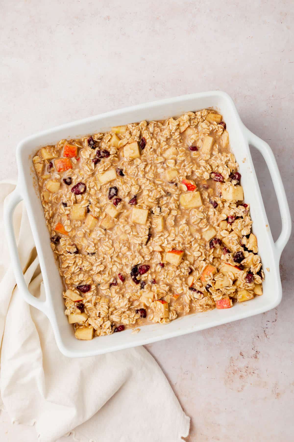 An oatmeal, apple and dried cranberry mixture in a square baking dish before baking in the oven.