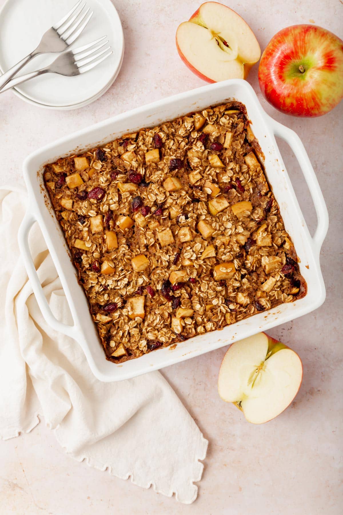 Gluten-free vegan apple baked oatmeal in a square baking dish with fresh apples surrounding the baking pan.
