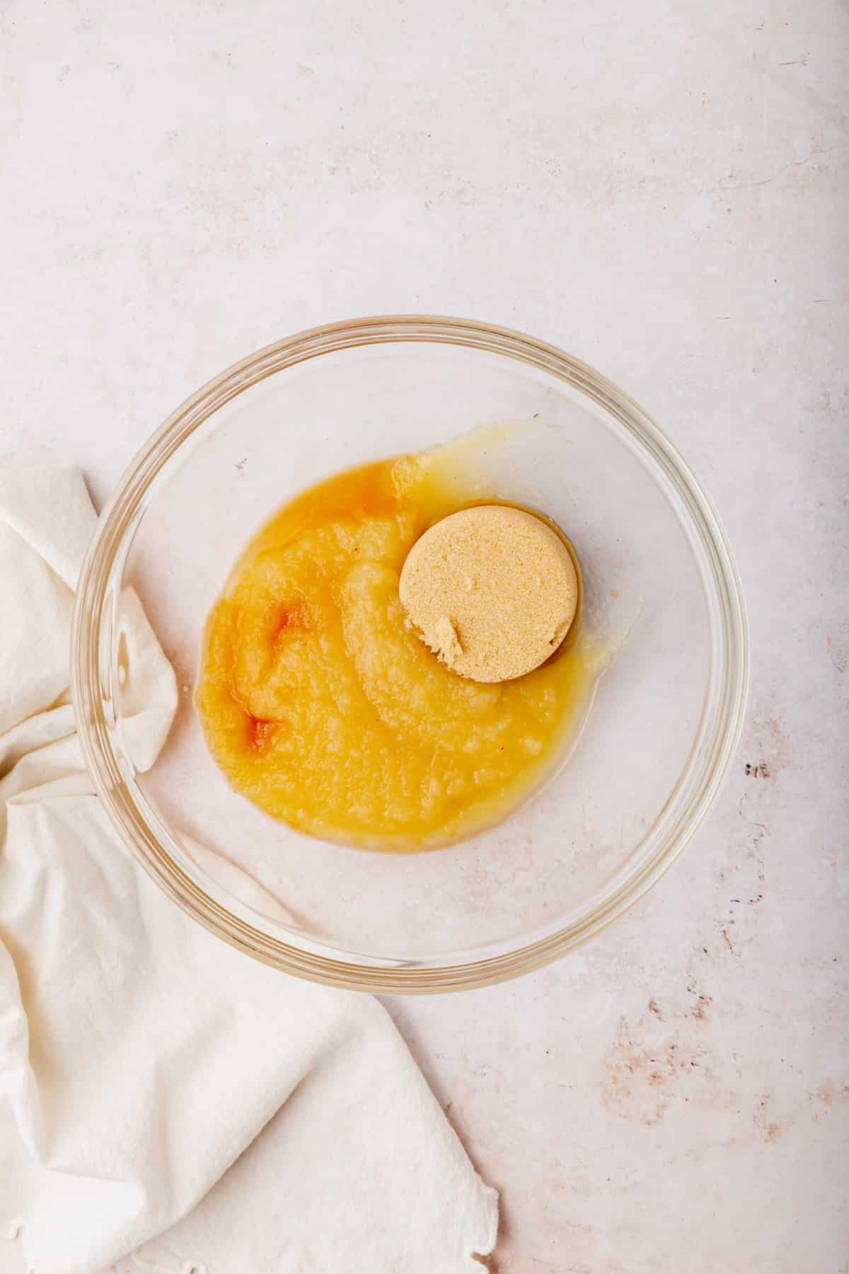 A glass mixing bowl with applesauce, brown sugar and vanilla in it before mixing together.