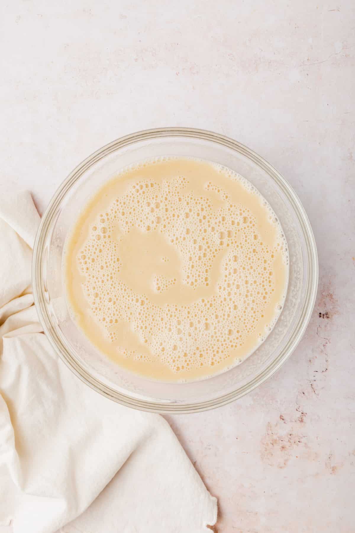 A glass mixing bowl with an almond milk mixture in it that has been mixed together.