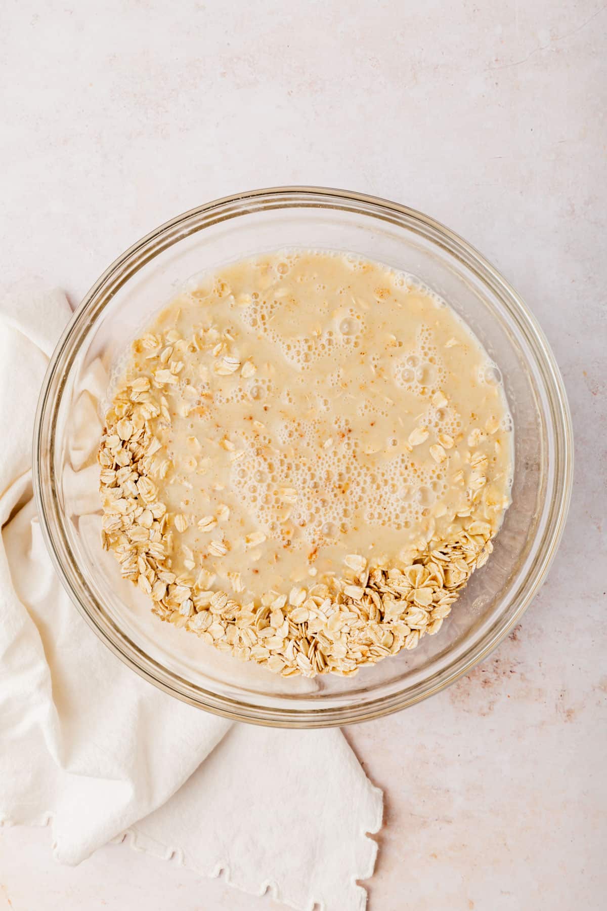 A glass mixing bowl with gluten-free oats topped with an almond milk mixture before mixing together.