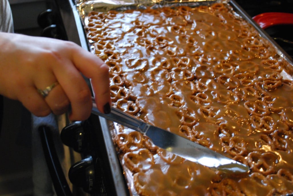 A baking sheet with gluten-free pretzels on it that are being covered in caramel sauce.