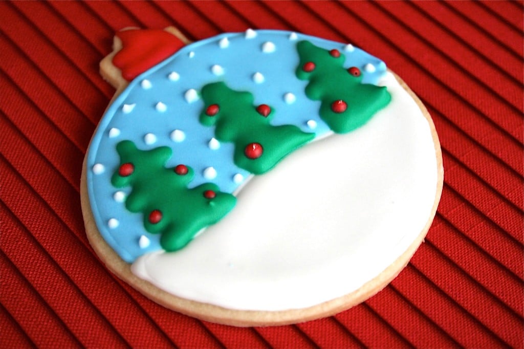 A snowglobe ornament sugar cookie on a red placemat.