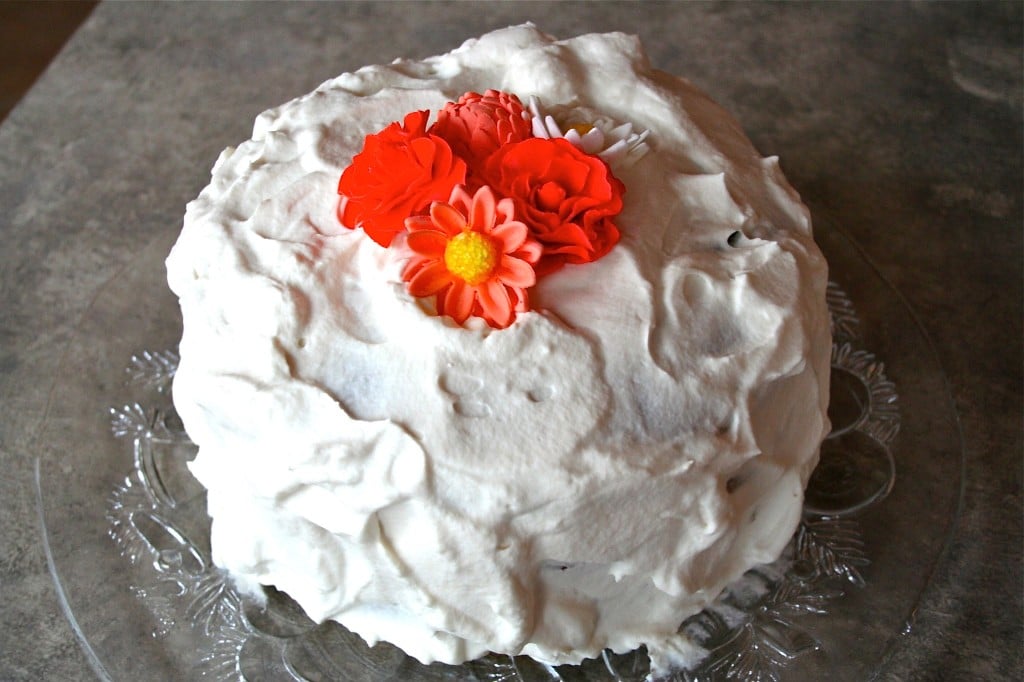 A cake topped with whipped cream and fondant flowers.
